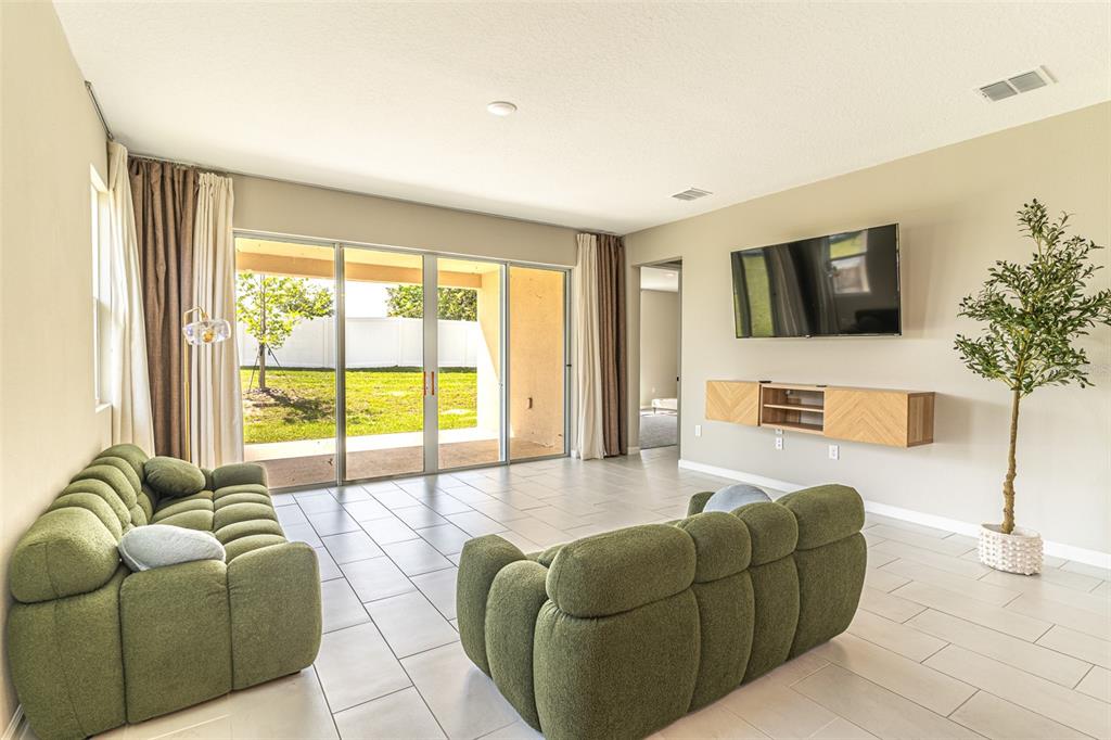 A living room features two green sofas, a wall-mounted television, and sliding glass patio doors — 148 HILLTOP BLOOM LOOP, HAINES CITY, FL
