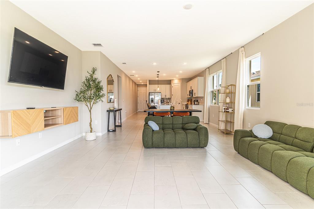 An open-concept living room features light tile flooring, two green modular sofas, and a kitchen — 148 HILLTOP BLOOM LOOP, HAINES CITY, FL