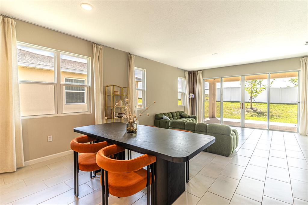 A dining area with a black table and orange chairs opens into a living room — 148 HILLTOP BLOOM LOOP, HAINES CITY, FL