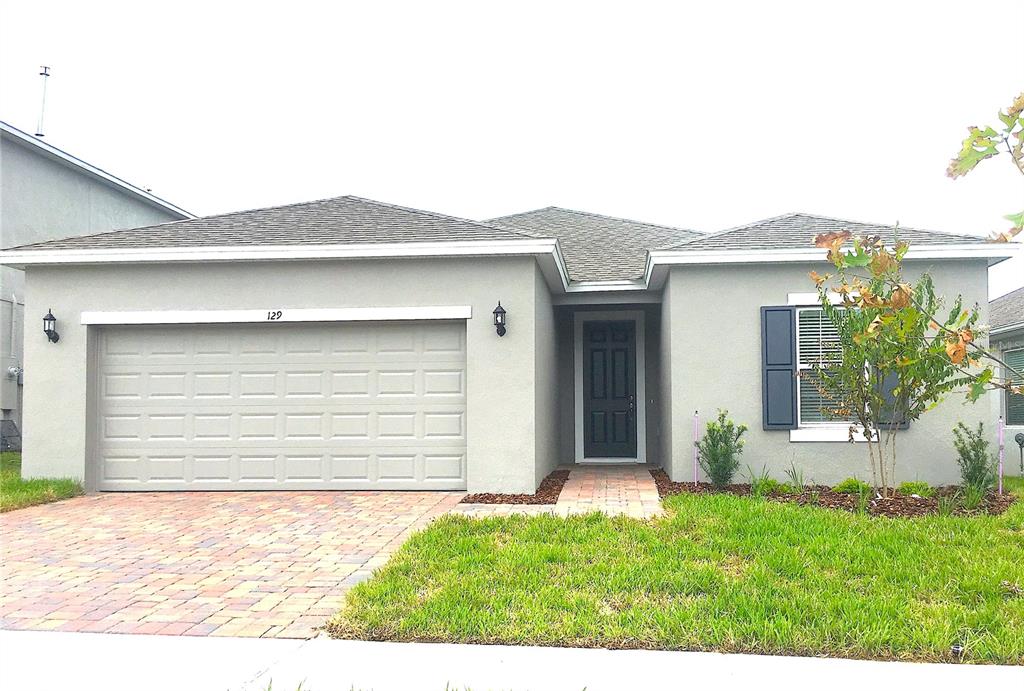 A single-story house with a gray stucco exterior, a two-car garage, and a brick driveway — 129 BELLA VERANO WAY, DAVENPORT, FL