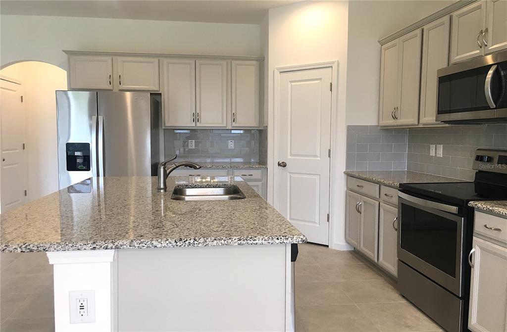 A kitchen features light gray cabinets, granite countertops, stainless steel appliances, and a center island — 129 BELLA VERANO WAY, DAVENPORT, FL