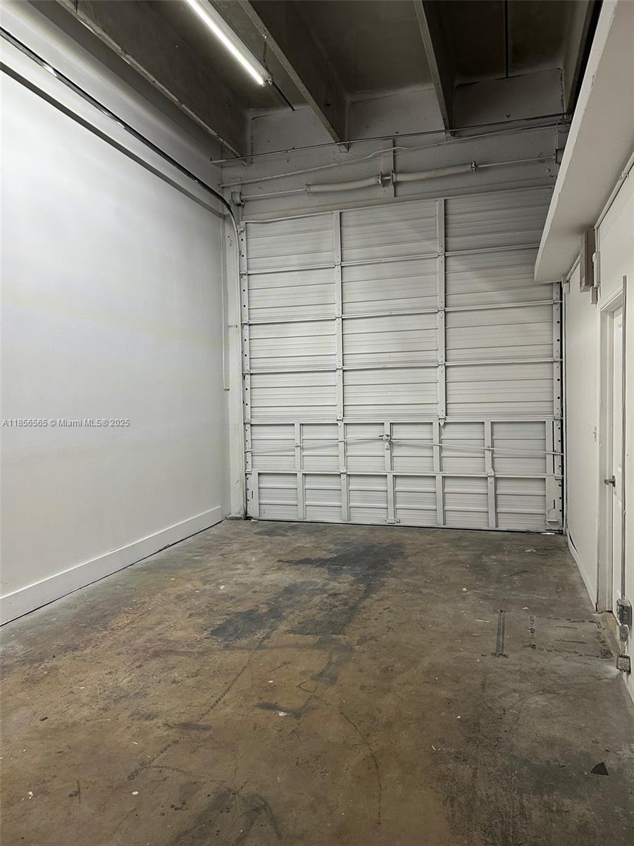 This industrial space features a concrete floor, white walls, and a large roll-up garage door — 470 Ansin Blvd # 470H, Hallandale Beach FL 33009, HALLANDALE BEACH, FL