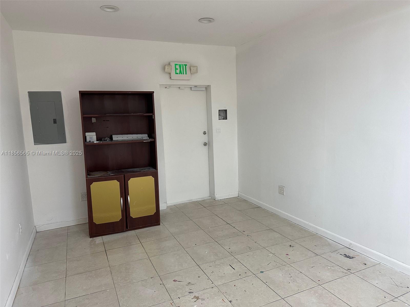 An empty room features white walls, tiled flooring, a dark wooden cabinet, and an exit door — 470 Ansin Blvd # 470H, Hallandale Beach FL 33009, HALLANDALE BEACH, FL