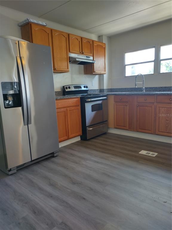 A kitchen features stainless steel appliances, wood cabinets, granite countertops, and gray wood-look flooring — 2031 LULLABY DRIVE, HOLIDAY, FL