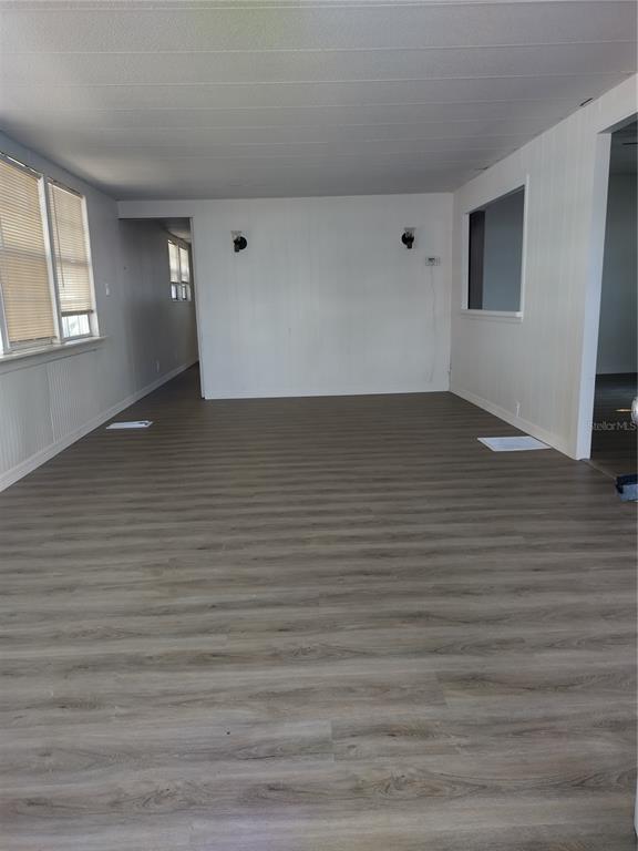 An empty room features wood-look vinyl flooring, white paneled walls, and two wall-mounted light fixtures — 2031 LULLABY DRIVE, HOLIDAY, FL