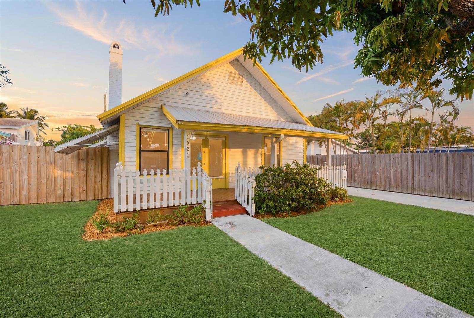 A white cottage with yellow trim and a picket fence sits on a grassy lawn — 1021 S N Street, FL 33460, FL
