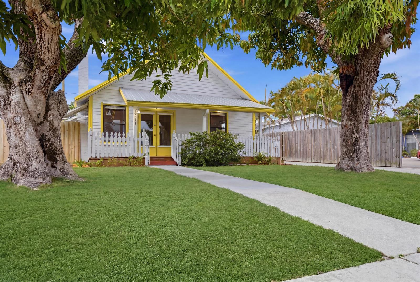 A white house with yellow trim and a picket fence sits behind a grassy lawn — 1021 S N Street, FL 33460, FL