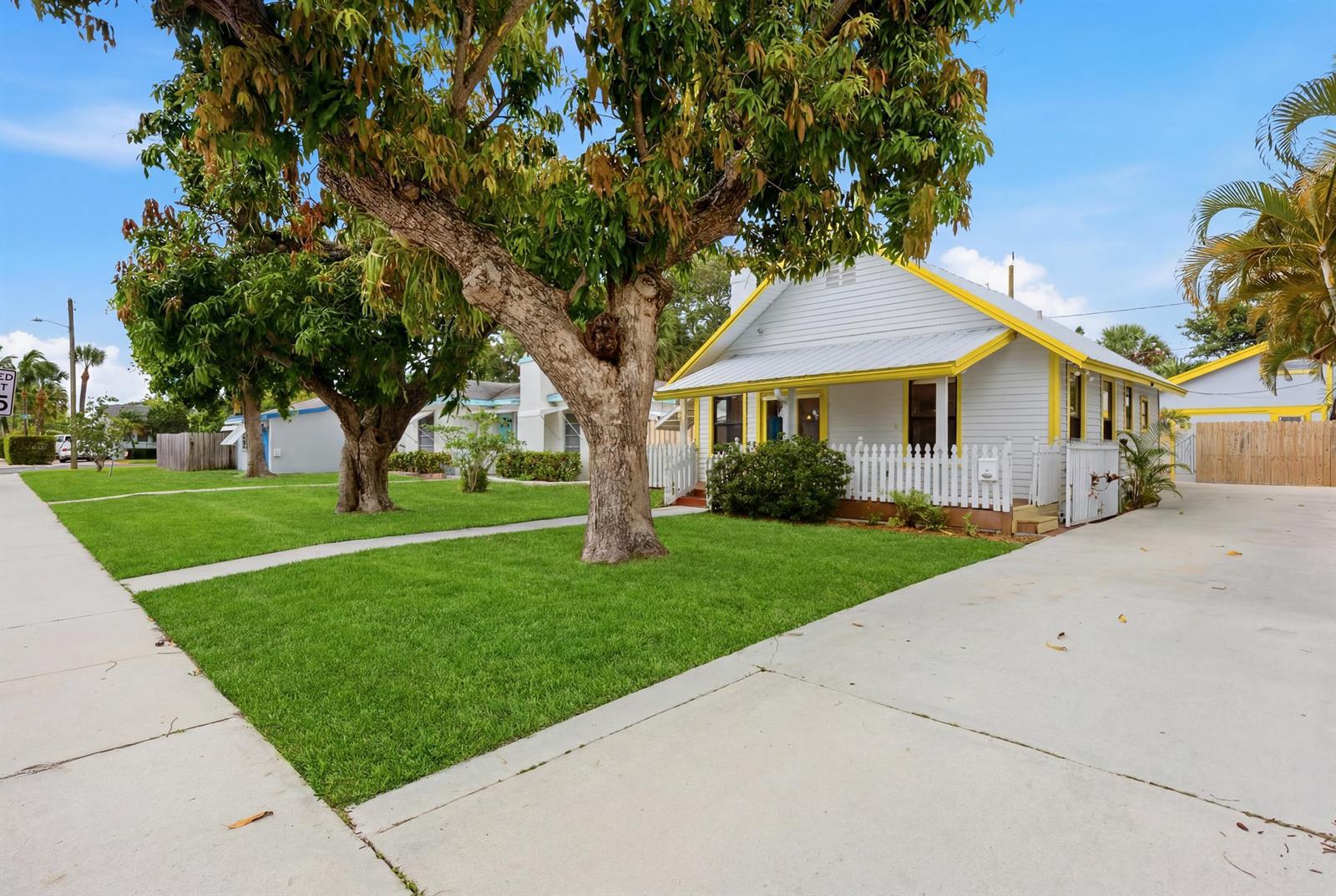 A light-colored cottage with yellow trim features a white picket fence and a concrete driveway — 1021 S N Street, FL 33460, FL