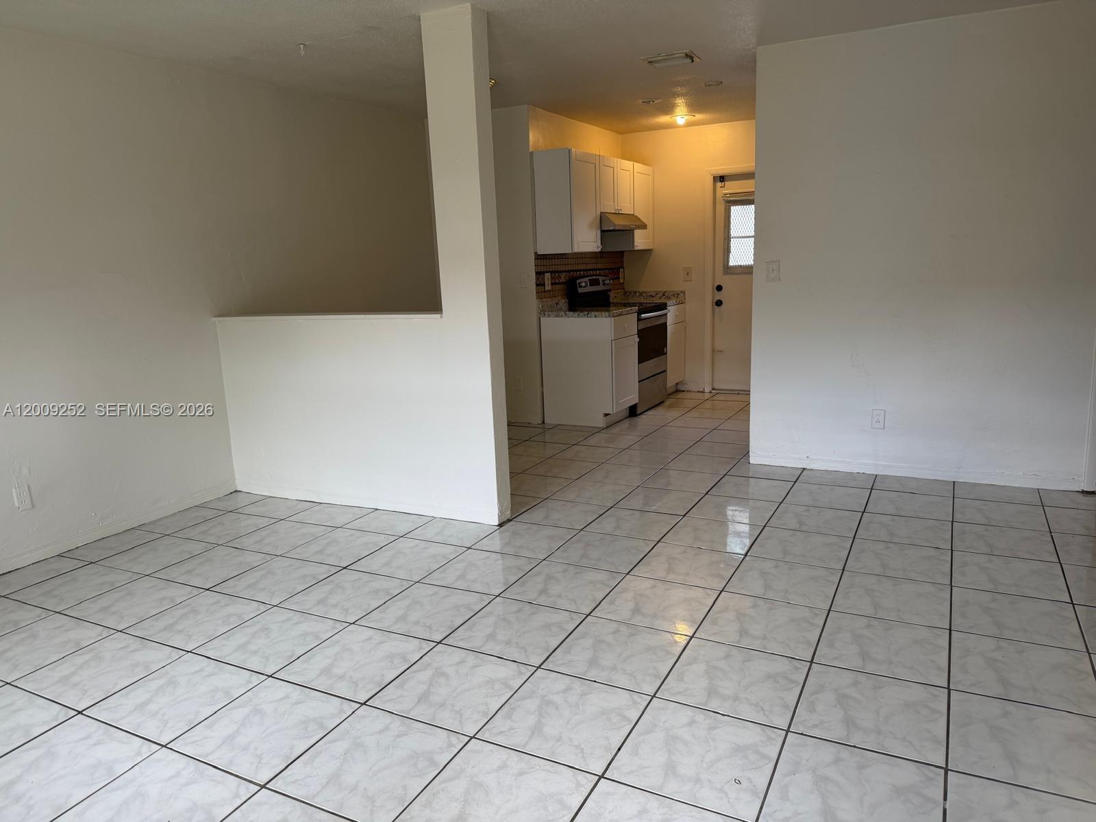 A kitchen with white cabinets and tiled floors is visible from an open living area — 728 SW 7th St # 2, Hallandale Beach FL 33009, HALLANDALE BEACH, FL