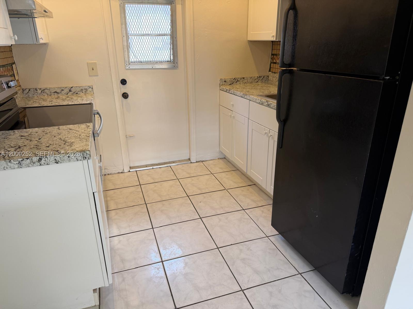 A kitchen features white cabinets, granite countertops, a black refrigerator, and light-colored floor tiles — 728 SW 7th St # 2, Hallandale Beach FL 33009, HALLANDALE BEACH, FL
