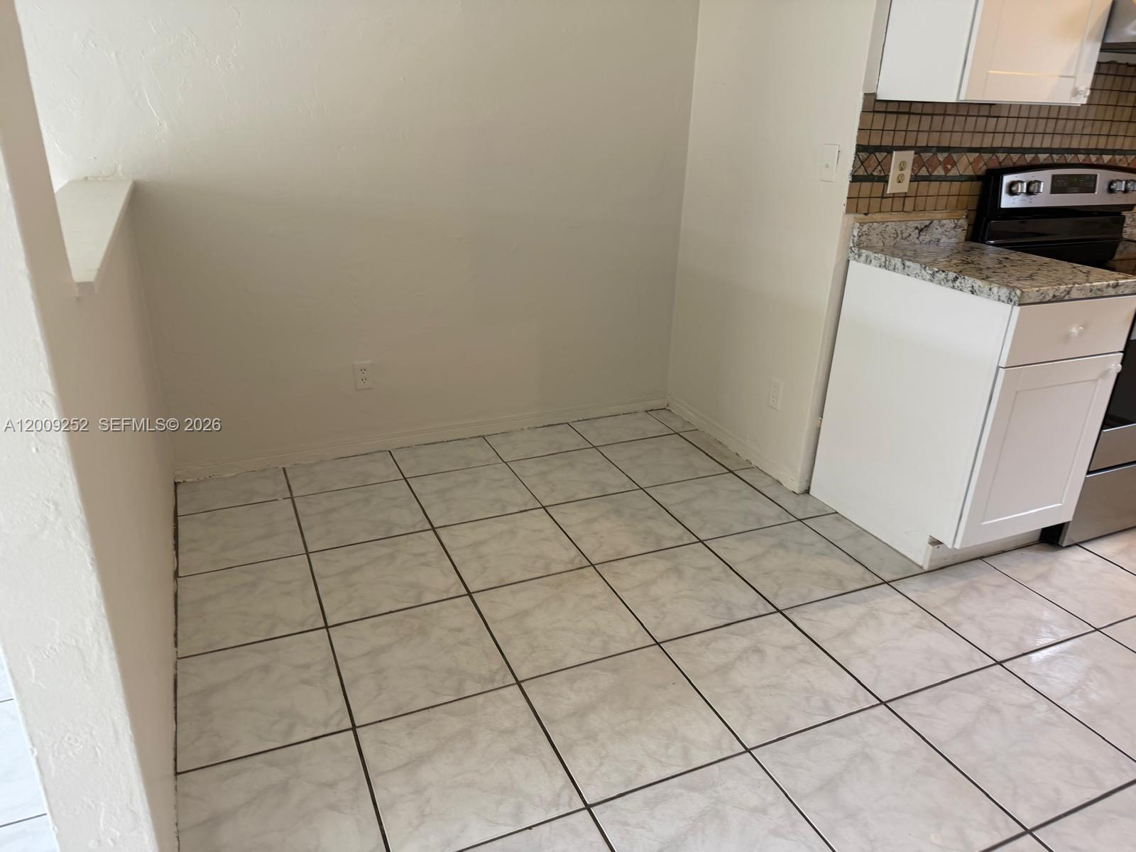 A kitchen area features white cabinets, granite countertops, a black stove, and light tiled flooring — 728 SW 7th St # 2, Hallandale Beach FL 33009, HALLANDALE BEACH, FL