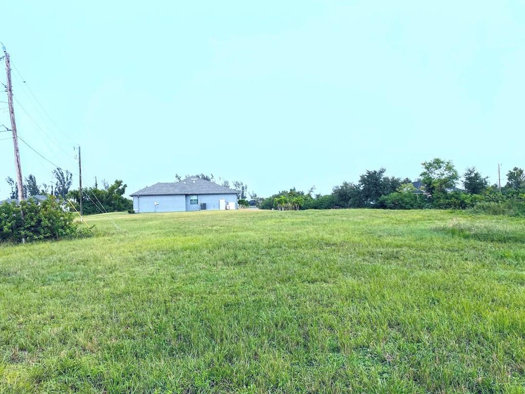 A large, grassy vacant lot sits in front of a single-story house under a clear sky — 809 NW 29TH AVE, CAPE CORAL, FL