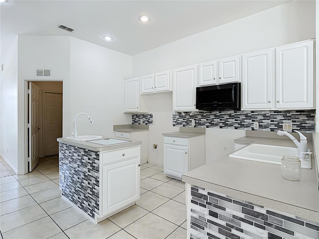 A kitchen features white cabinets, gray countertops, a tiled island, and a mosaic backsplash — 957 VIA BIANCA DRIVE, DAVENPORT, FL