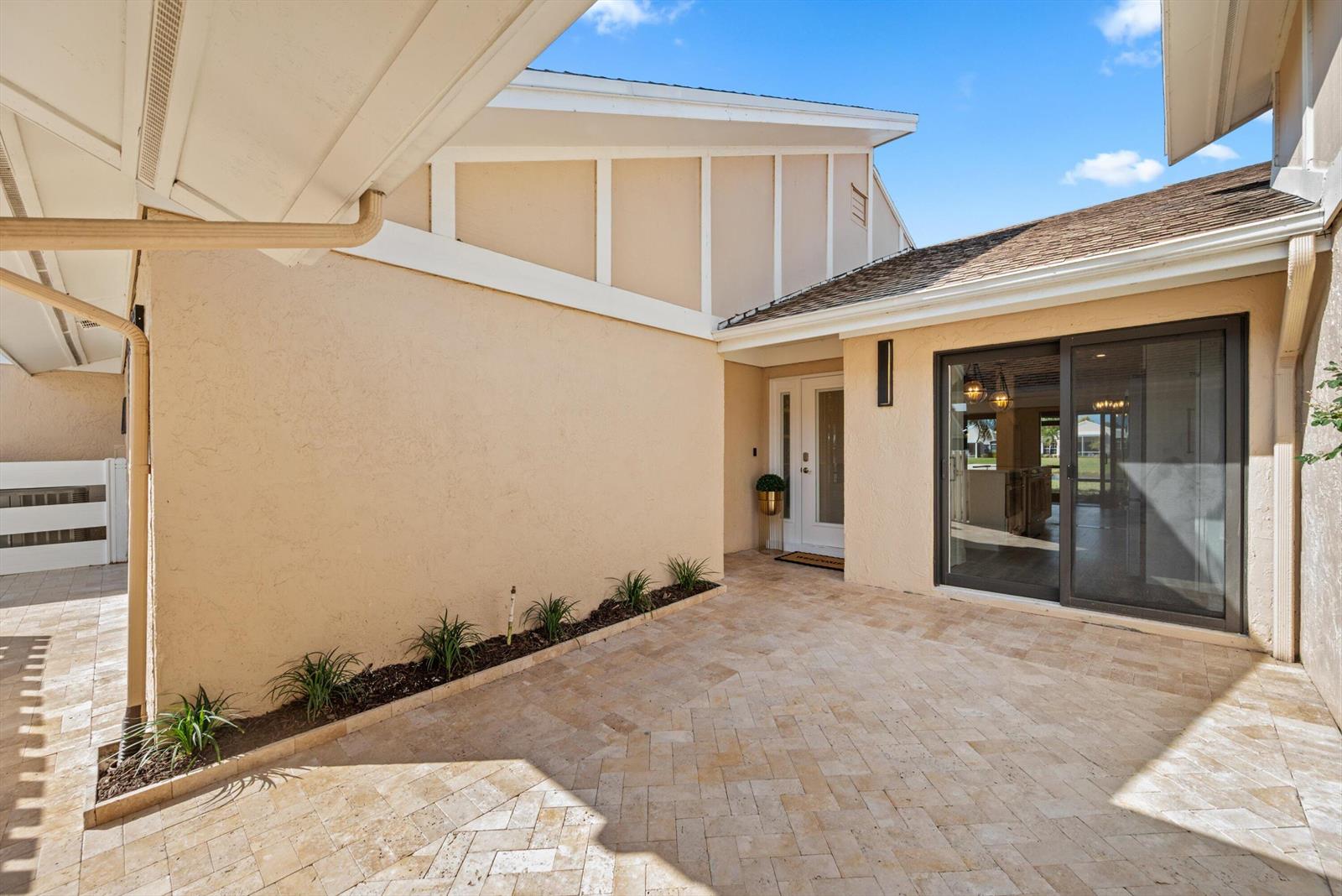 A beige stucco house exterior features a paved courtyard, sliding glass doors, and a front entrance — 3733 Cape Pointe Circle, Jupiter FL 33477, JUPITER, FL
