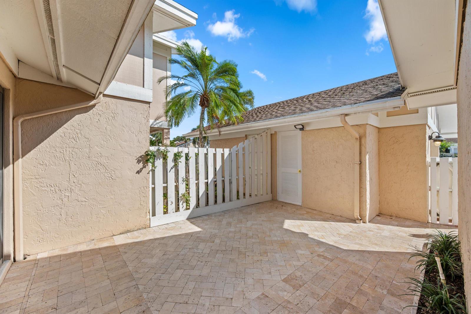 A paved courtyard features a white wooden fence, a storage door, and a palm tree — 3733 Cape Pointe Circle, Jupiter FL 33477, JUPITER, FL