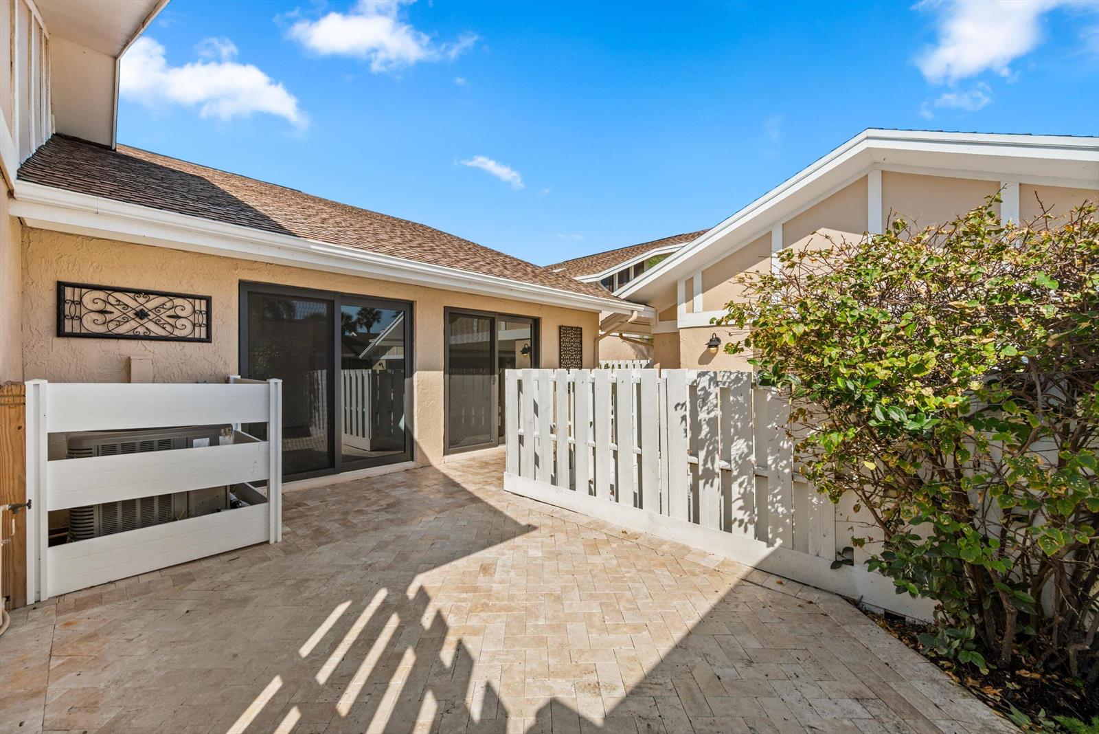 A paved patio area features a white privacy fence, sliding glass doors, and exterior walls — 3733 Cape Pointe Circle, Jupiter FL 33477, JUPITER, FL