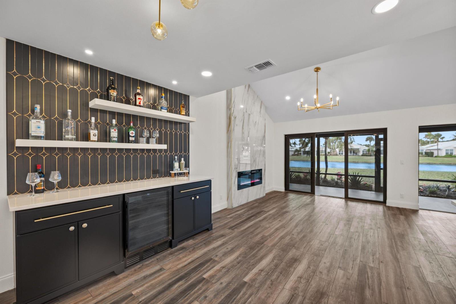 A modern bar area with dark cabinetry, floating shelves, and a fireplace overlooks a lake — 3733 Cape Pointe Circle, Jupiter FL 33477, JUPITER, FL