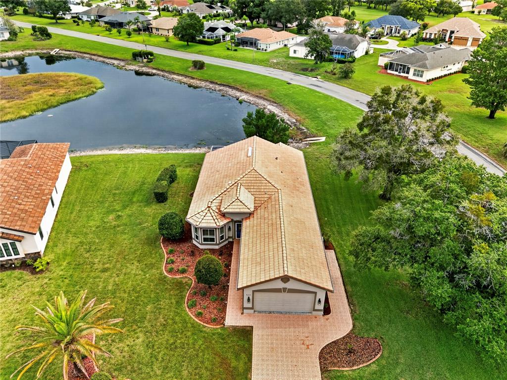 An aerial view of a single-story house with a tiled roof, driveway, and backyard pond — 9257 BONNIE COVE DRIVE, WEEKI WACHEE, FL