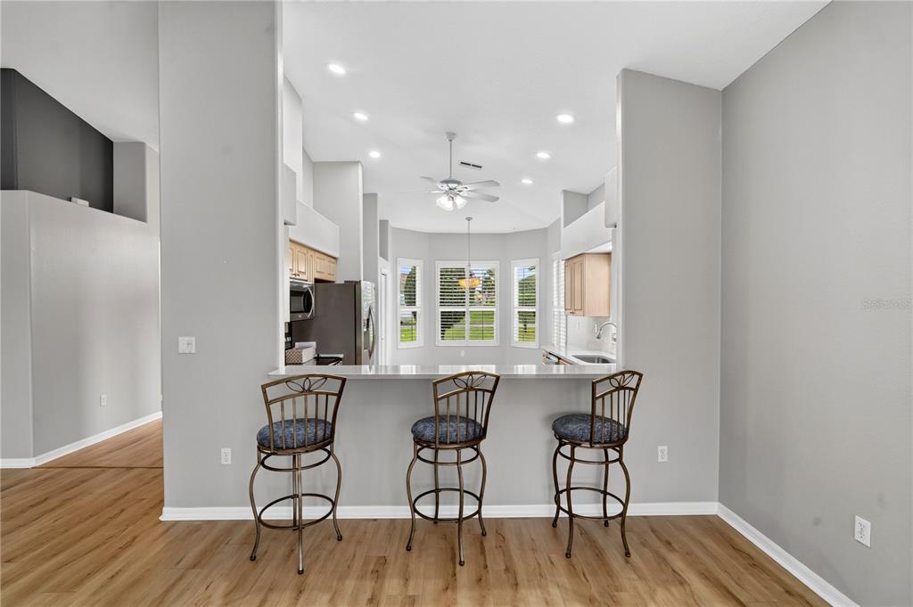 A kitchen with a breakfast bar, three stools, and light wood flooring — 9257 BONNIE COVE DRIVE, WEEKI WACHEE, FL