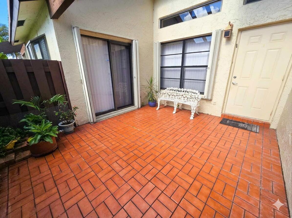 A patio with orange brick pavers, a white metal bench, and a sliding glass door — 14103 Nesting Way # C, Delray Beach FL 33484, DELRAY BEACH, FL