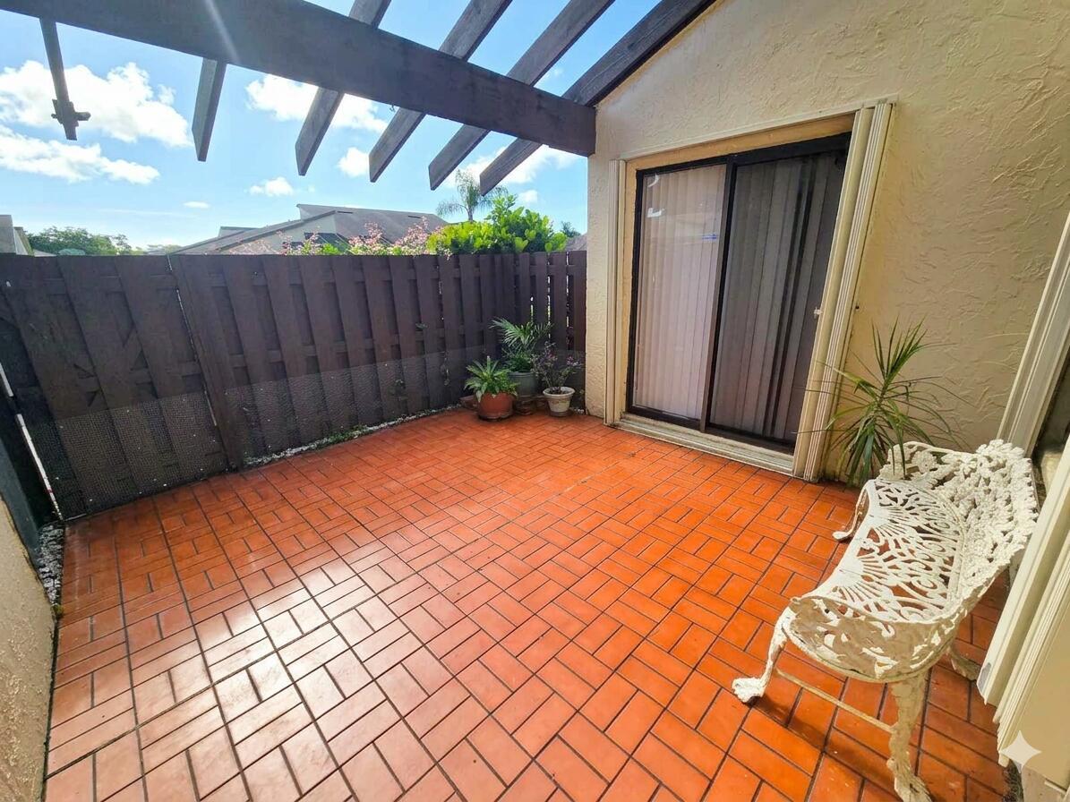 A patio with orange tile flooring, a white metal bench, and a wooden pergola overhead — 14103 Nesting Way # C, Delray Beach FL 33484, DELRAY BEACH, FL