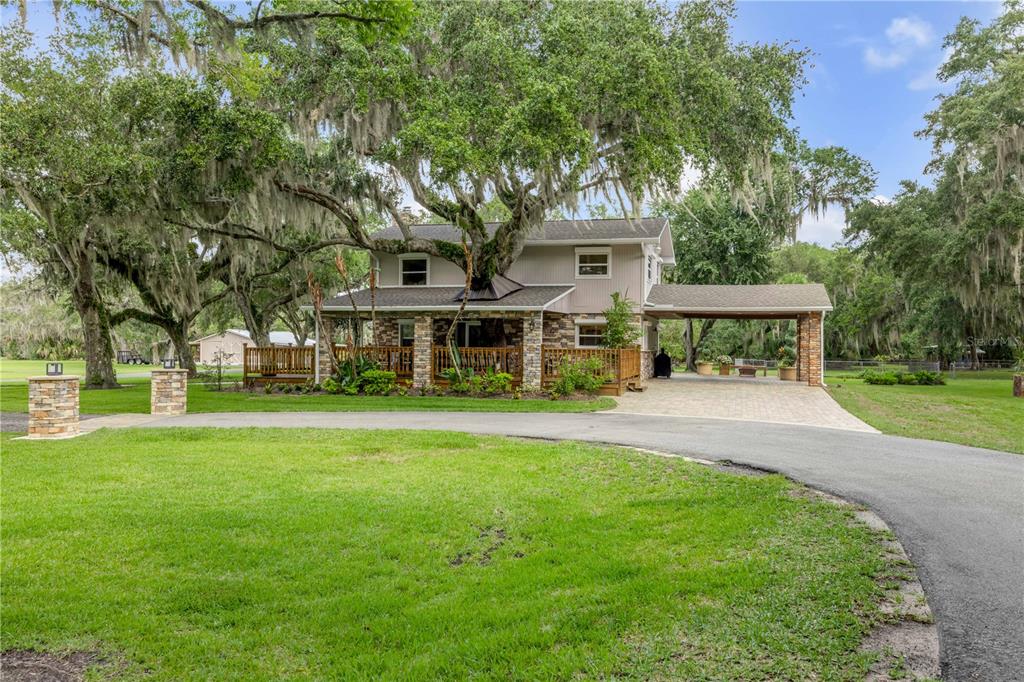 A two-story house with a stone-accented porch and a large tree growing through the roof — 800 HIDDEN OAKS LANE, OAK HILL, FL