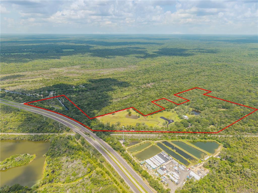 An aerial view shows a large, forested property outlined in red next to a highway — 800 HIDDEN OAKS LANE, OAK HILL, FL