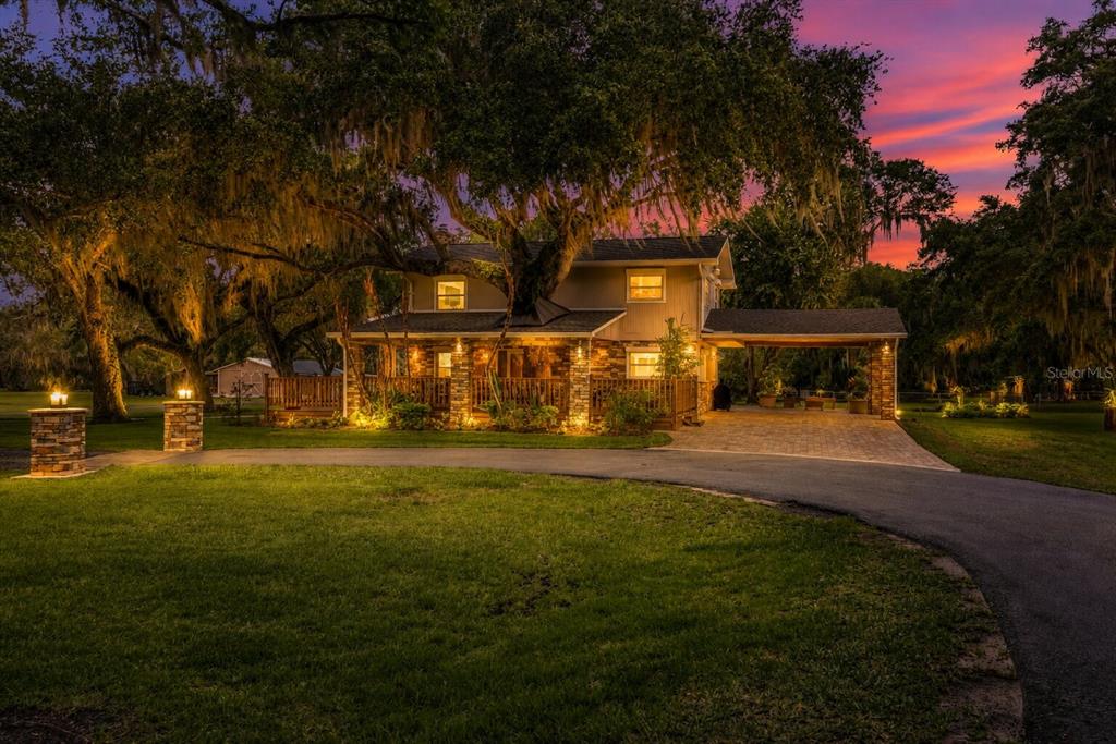 A two-story house with a large tree growing through the roof at dusk — 800 HIDDEN OAKS LANE, OAK HILL, FL