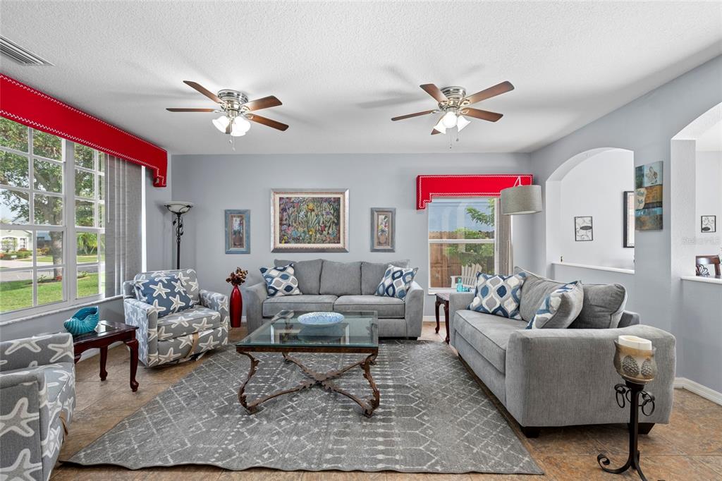 A living room features two grey sofas, a patterned armchair, and two ceiling fans — 7020 49TH PLACE E, PALMETTO, FL