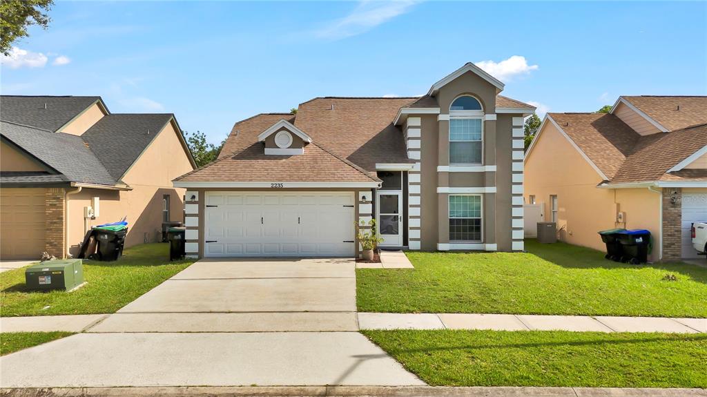 A two-story suburban house with a tan stucco exterior, brown shingled roof, and two-car garage — 2235 MEADOWMOUSE STREET, ORLANDO, FL