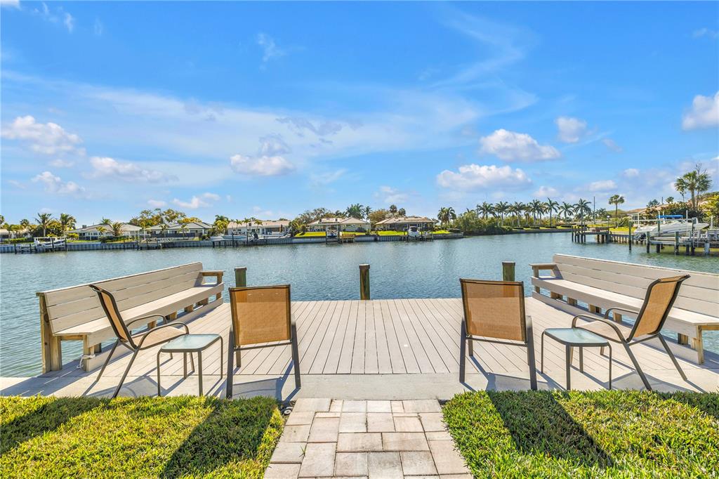 A wooden dock with chairs and benches overlooks a canal with houses in the distance — 1964 MASSACHUSETTS AVENUE NE, ST PETERSBURG, FL