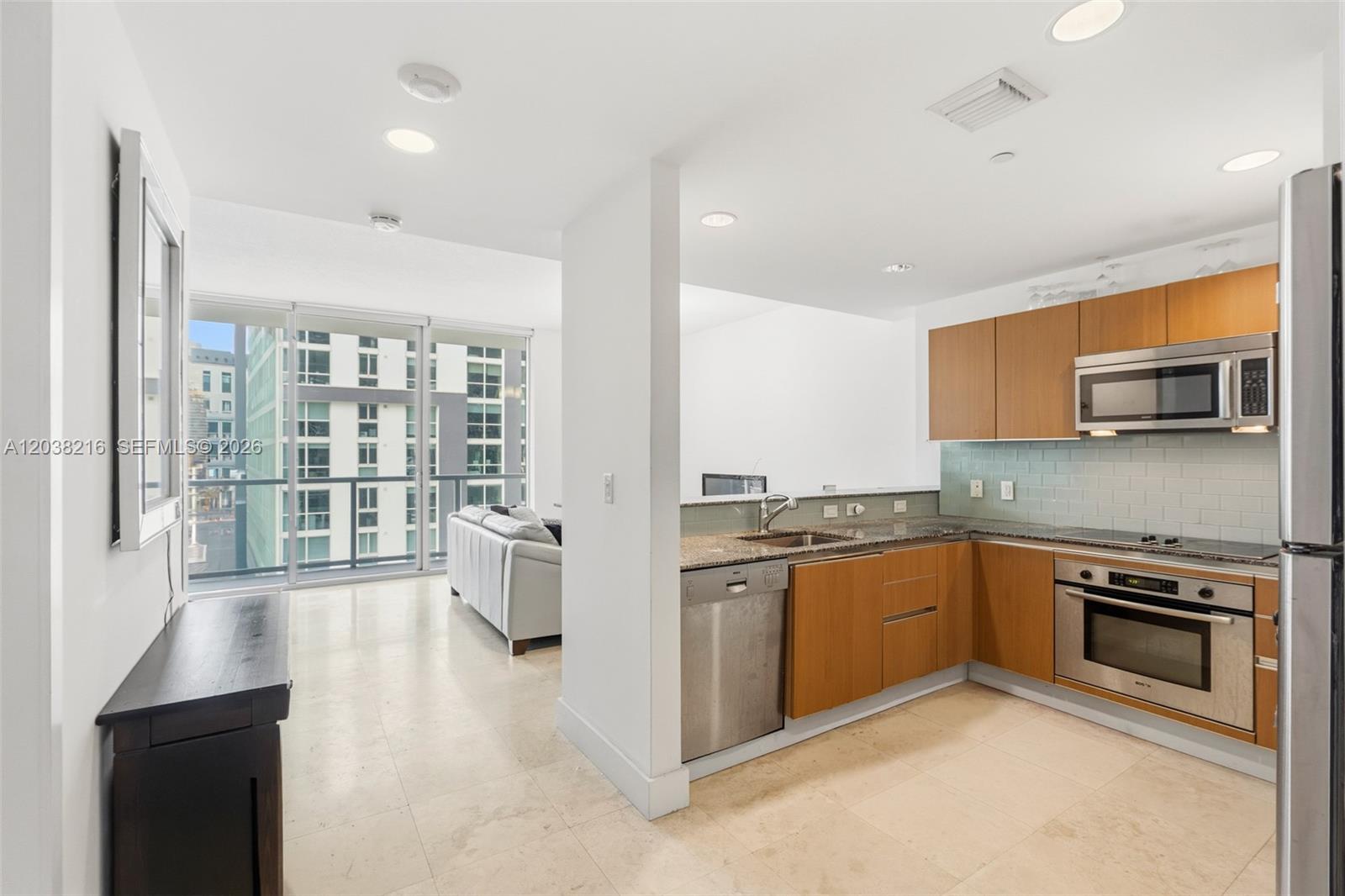 A kitchen with wood cabinets and stainless steel appliances opens to a living area — 1050 Brickell Ave # 2112, Miami FL 33131, MIAMI, FL