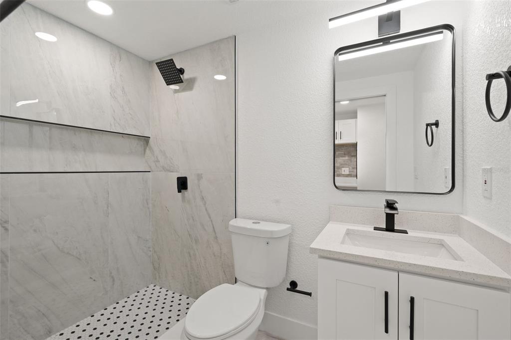 A modern bathroom features a glass-enclosed walk-in shower, a white vanity, and marble-look tile — 2008 OAKWOOD AVENUE UNIT B, TAMPA, FL