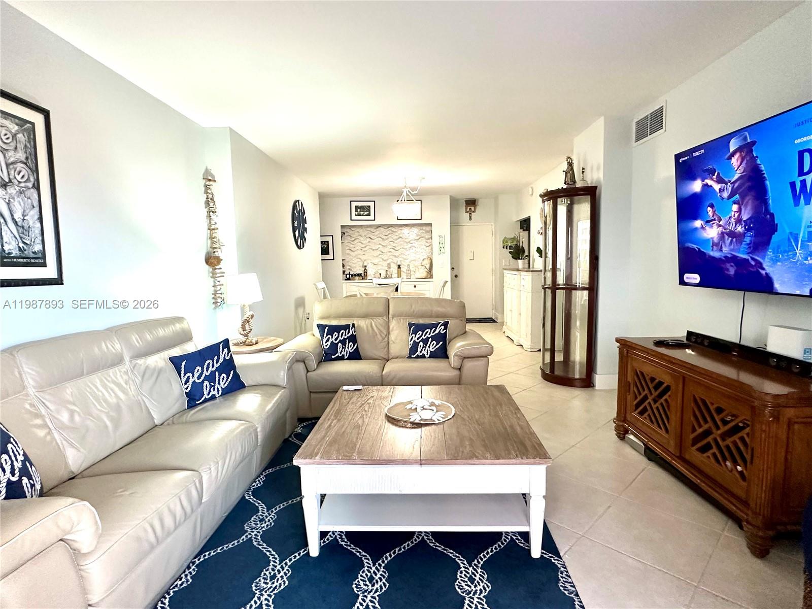 A living room features a beige sofa, a wooden coffee table, and a wall-mounted television — 1950 S Ocean Dr # 2C, Hallandale Beach FL 33009, HALLANDALE BEACH, FL