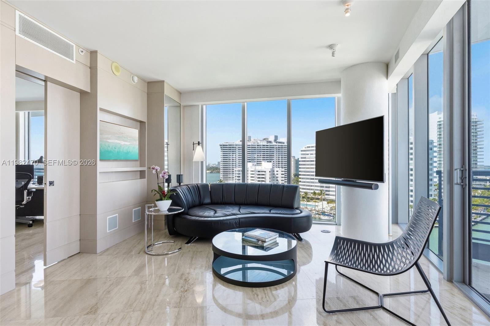 A modern living room features a black curved sofa, glass coffee table, and floor-to-ceiling windows — 1445 16th St # 1101, Miami Beach FL 33139, MIAMI BEACH, FL