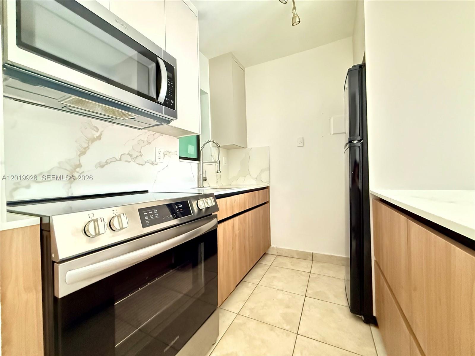 A galley kitchen features light wood cabinets, white marble-style backsplashes, and stainless steel appliances — 1530 SW 2nd St # 304, Miami FL 33135, MIAMI, FL