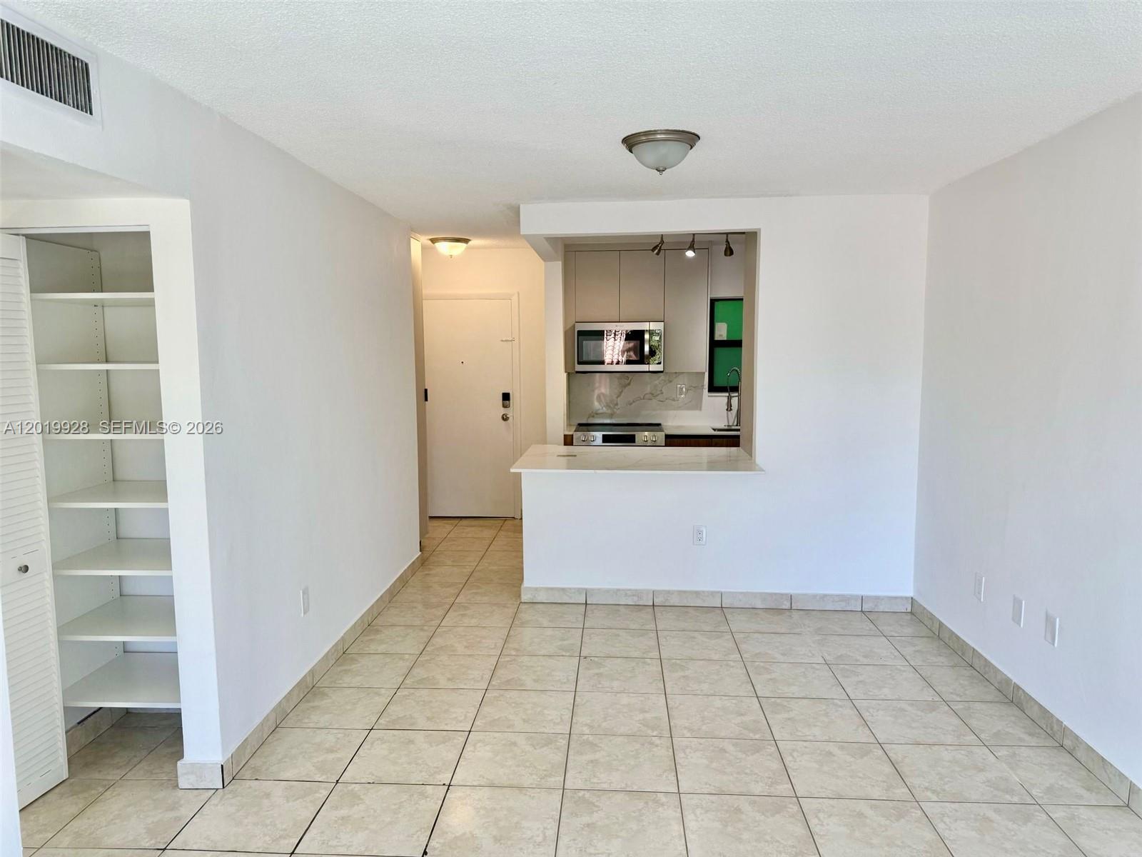 A kitchen with a breakfast bar opens into a tiled living area with shelving — 1530 SW 2nd St # 304, Miami FL 33135, MIAMI, FL