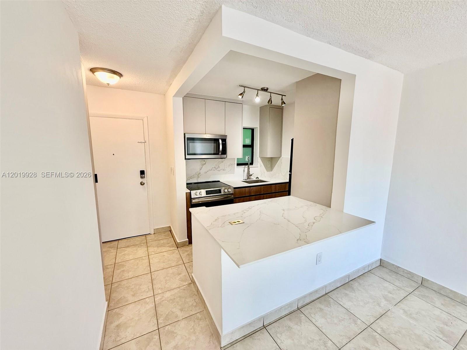 A kitchen with a white quartz peninsula, stainless steel appliances, and light-colored tile flooring — 1530 SW 2nd St # 304, Miami FL 33135, MIAMI, FL