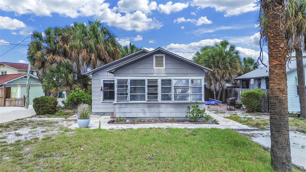 A gray, single-story house with a front porch and louvered windows sits on a grassy lot — 130 90TH AVENUE, TREASURE ISLAND, FL