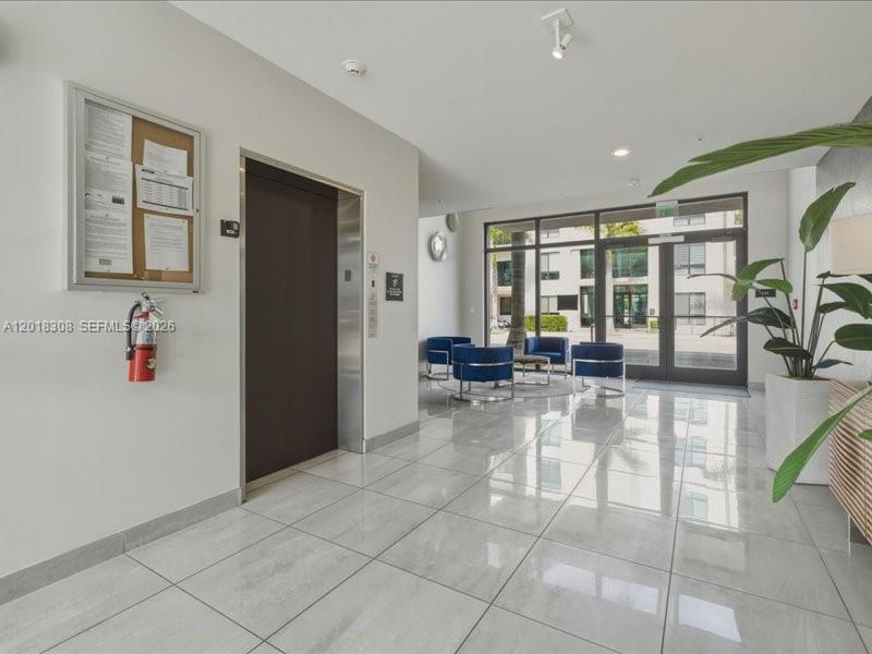 A modern lobby features a dark elevator door, a bulletin board, and blue seating — 8201 NW 41st St # 205, Doral FL 33166, DORAL, FL