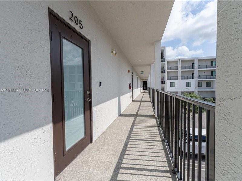 An outdoor apartment hallway features a brown door labeled 205 and a black metal railing — 8201 NW 41st St # 205, Doral FL 33166, DORAL, FL