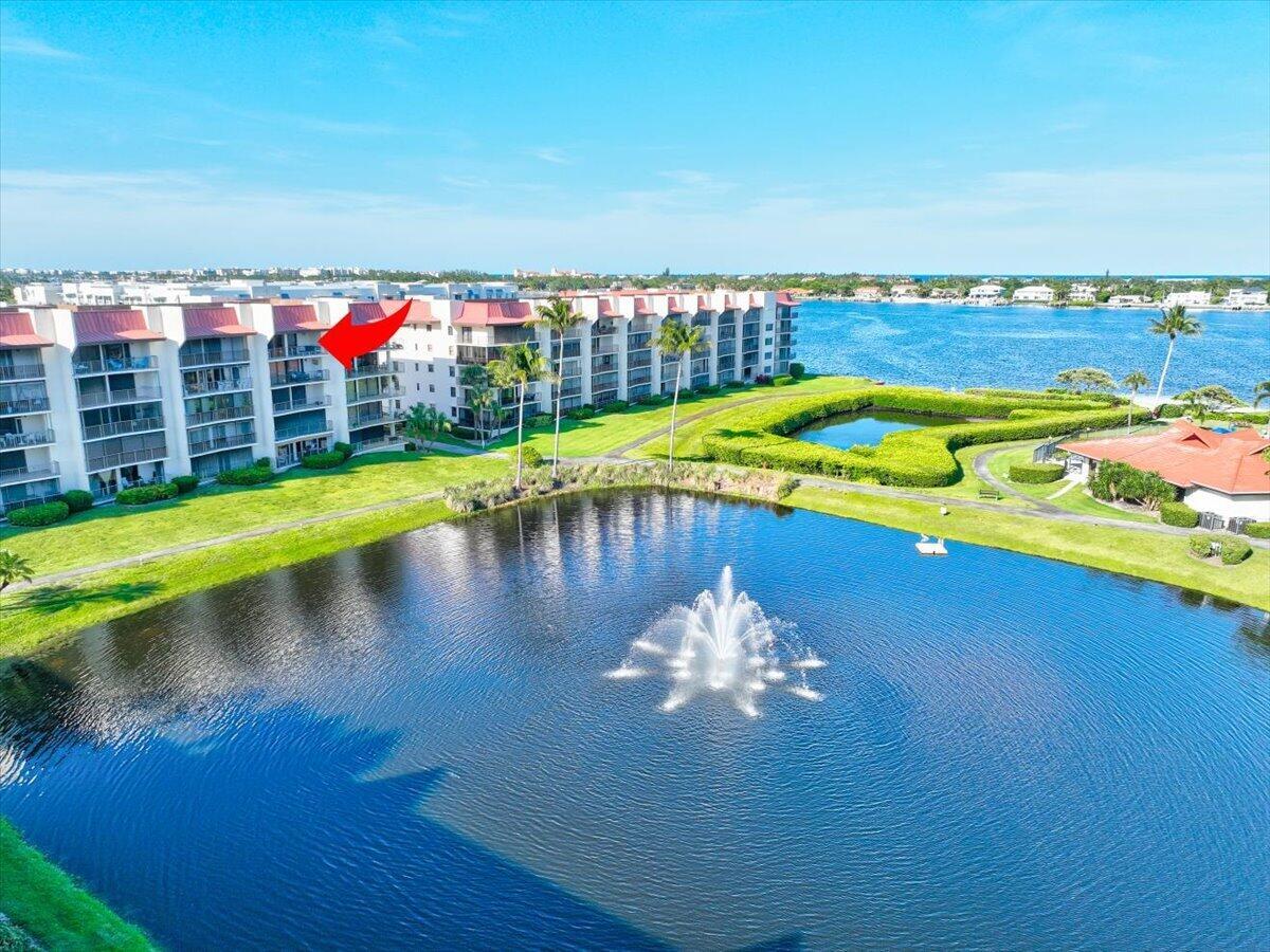 An aerial view shows a multi-story apartment building overlooking a pond with a fountain — 7030 Half Moon Circle # 515, Hypoluxo FL 33462, HYPOLUXO, FL