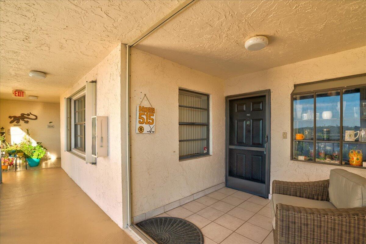 An outdoor apartment entryway features a tiled floor, a dark door, and a wicker chair — 7030 Half Moon Circle # 515, Hypoluxo FL 33462, HYPOLUXO, FL