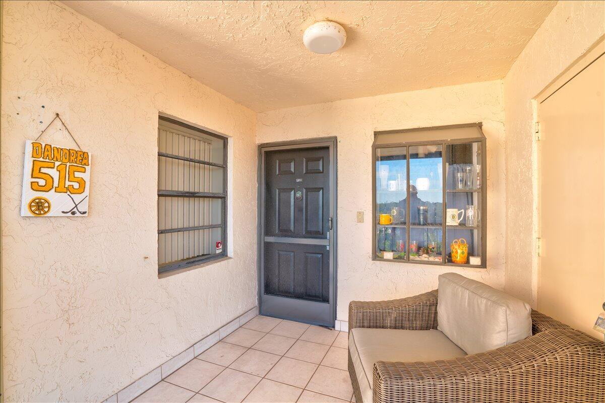 A covered patio features tiled flooring, a wicker chair, a wall-mounted display case, and decor — 7030 Half Moon Circle # 515, Hypoluxo FL 33462, HYPOLUXO, FL