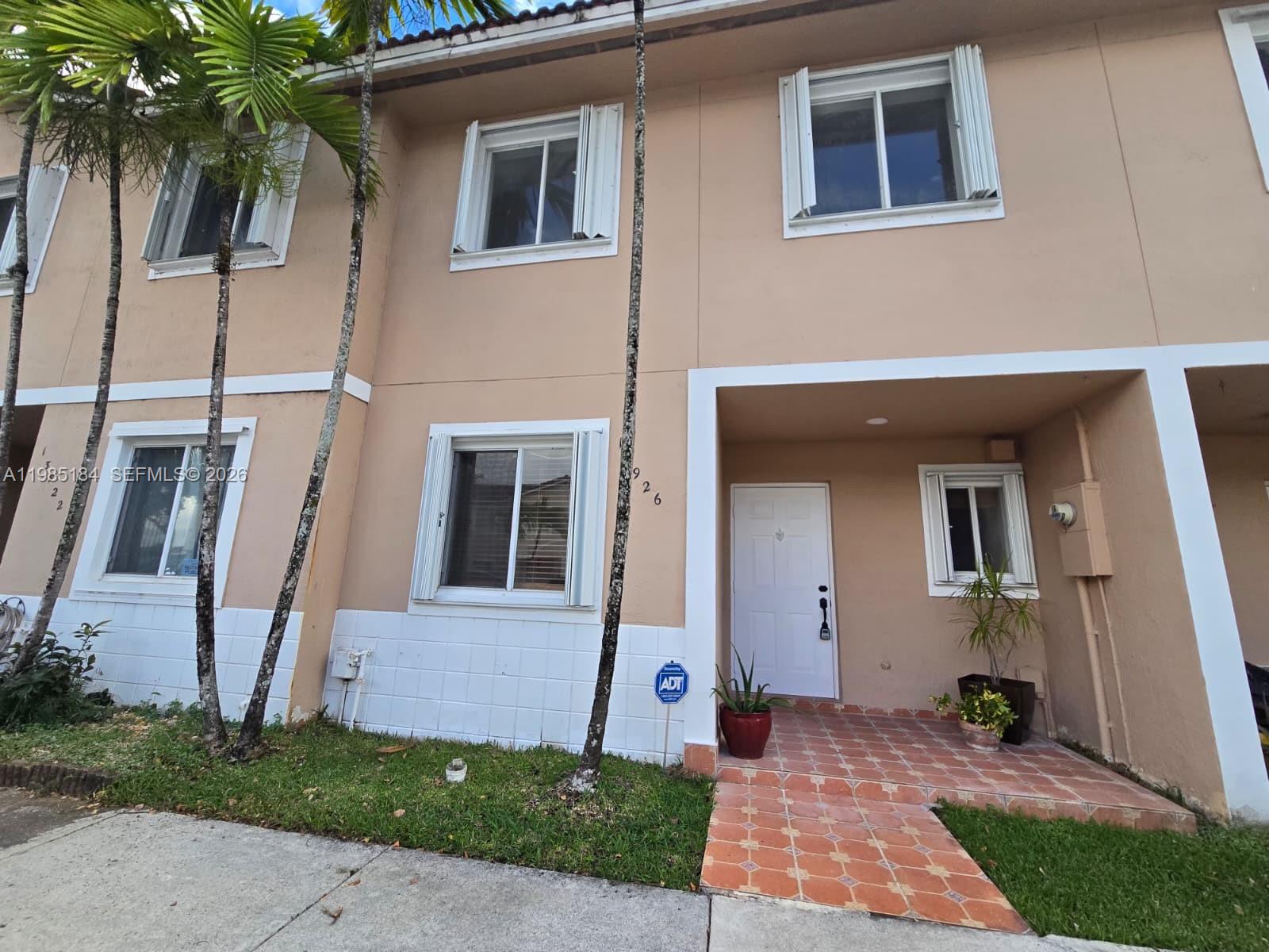 A two-story tan townhouse exterior features white trim, tiled entryway, and several palm trees — 13926 SW 175th Ter, Miami FL 33177, MIAMI, FL