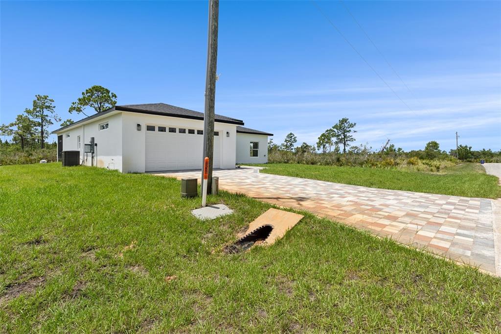 A white house with a paved driveway and a drainage pipe in the front yard — 7435 CASILLA STREET, SEBRING, FL