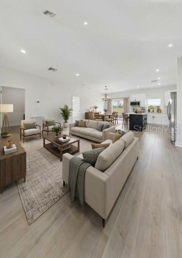 An open-concept living room features light wood flooring, neutral furniture, and a kitchen in back — 7435 CASILLA STREET, SEBRING, FL