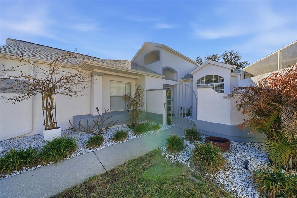 A white stucco house exterior features a concrete walkway leading to a gated courtyard entrance — 11008 CASA GRANDE, SPRING HILL, FL