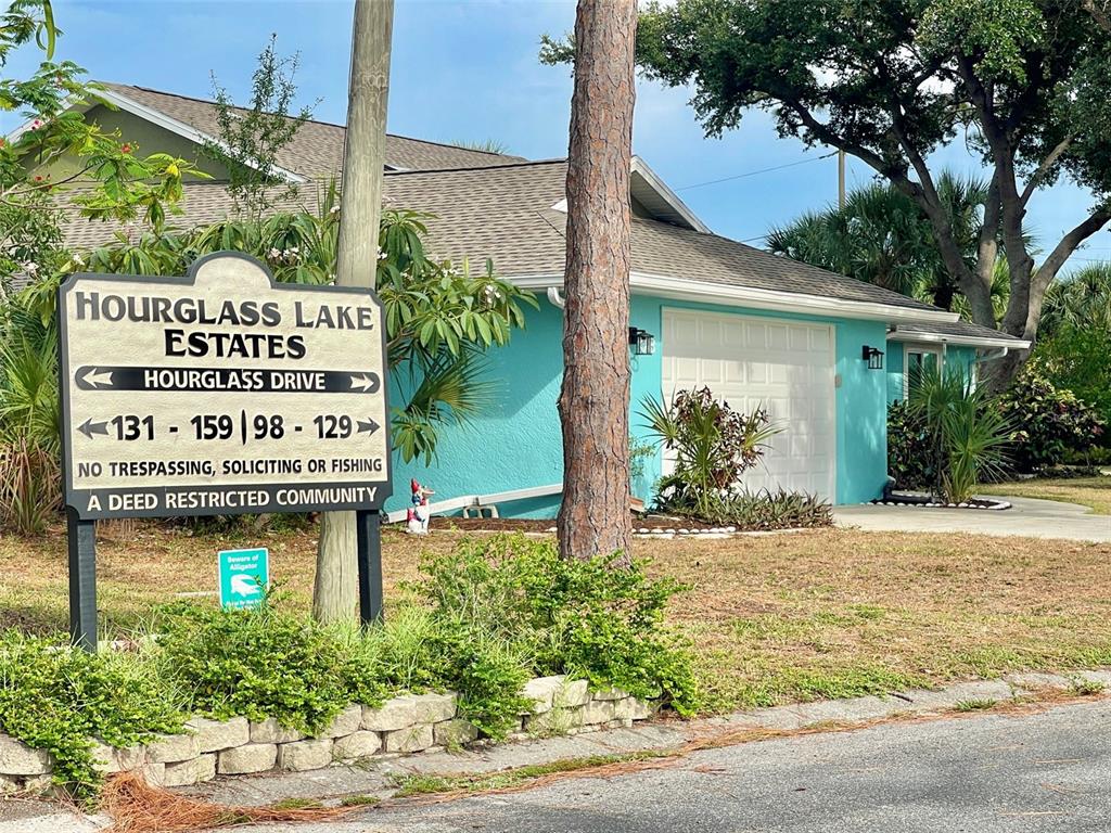A teal house with a white garage sits behind a community sign and tree — 98 HOURGLASS DRIVE, VENICE, FL