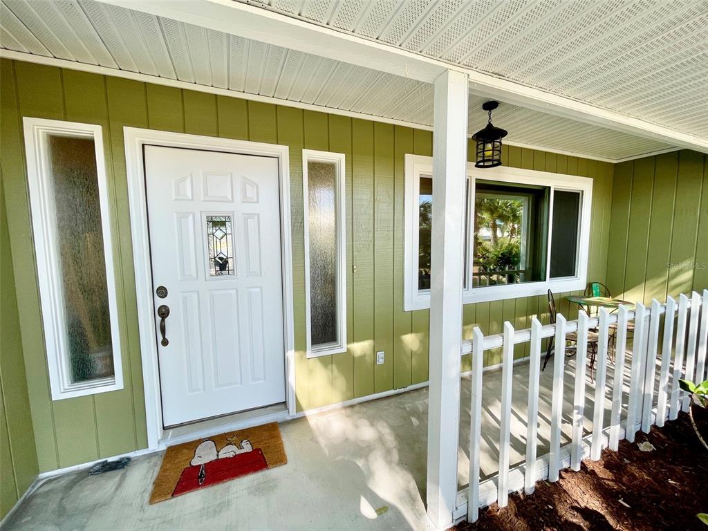 A white front door with side windows sits on a porch with green vertical siding — 98 HOURGLASS DRIVE, VENICE, FL